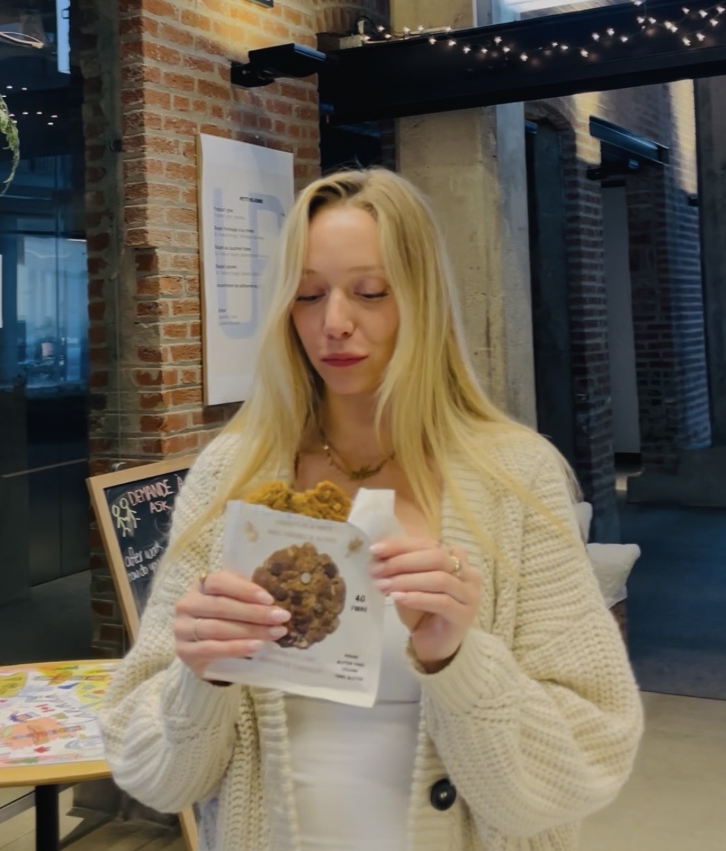 Blonde woman in a cream cardigan opening a Pick Me Up cookie package in a café