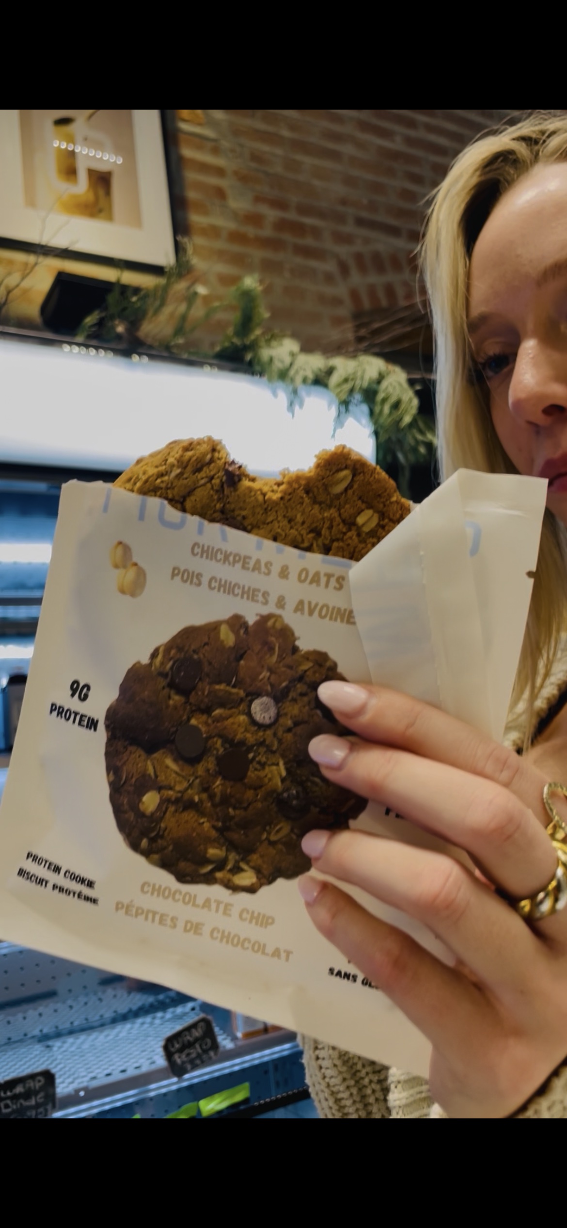 Blonde woman eating a Pick Me Up chocolate chip cookie