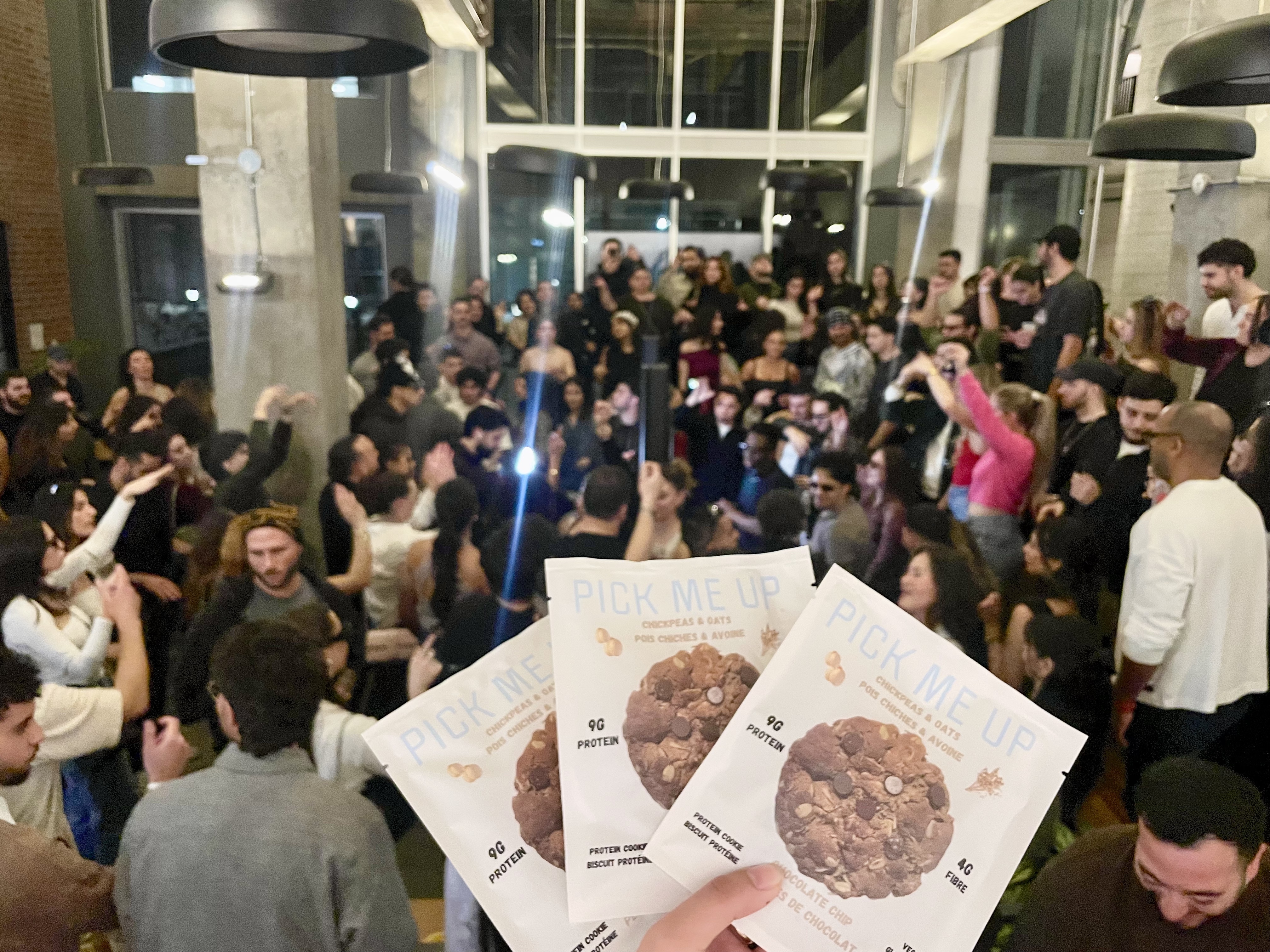 Crowd at an event with someone holding up Pick Me Up cookie packages in the foreground